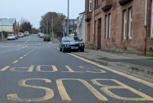 A dark blue car parked on a pavement in the middle of a bus stop