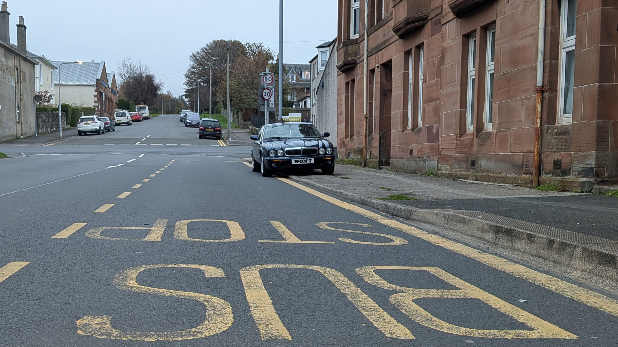 A dark blue car parked on a pavement in the middle of a bus stop